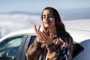 Young woman wearing a sweater and putting on sunblock in the winter for skin protection