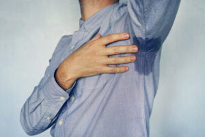 Person with visible underarm sweat stains on a blue shirt, showing excessive sweating related to hyperhidrosis.